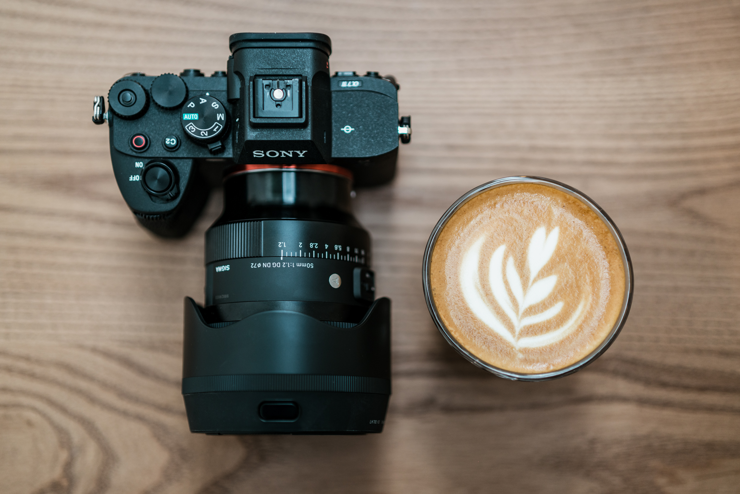 obiektyw Sigma 50 mm f/1.2 zamocowany do aparatu, obok na stole znajduje się kawa
